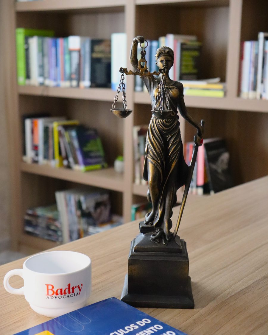 Escritório da Badry Advocacia: estatueta da Justiça, caneca da marca e livro de cálculos previdenciários